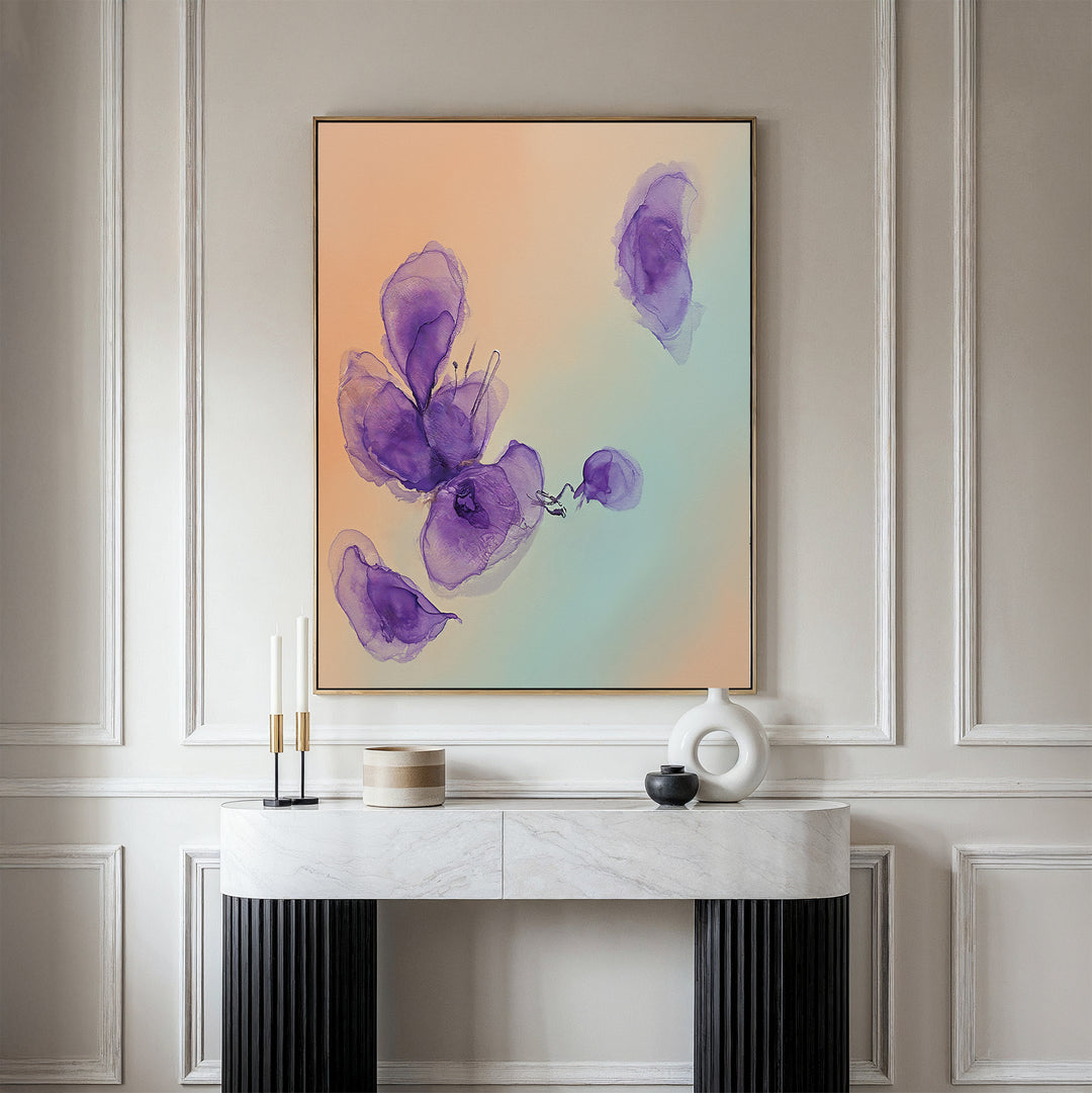 A modern, minimalist console table with decorative objects stands against a paneled wall, topped by the Violet Dreams Canvas Art - Vertical, which features abstract purple flowers on a soft pastel background.