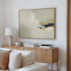 A modern living room features a light wood sideboard with stacked books, a lamp, and a bowl, while the Weathered Composition Canvas Art - Horizontal in neutral tones hangs above a beige sofa with white and cream pillows for an elegant look.