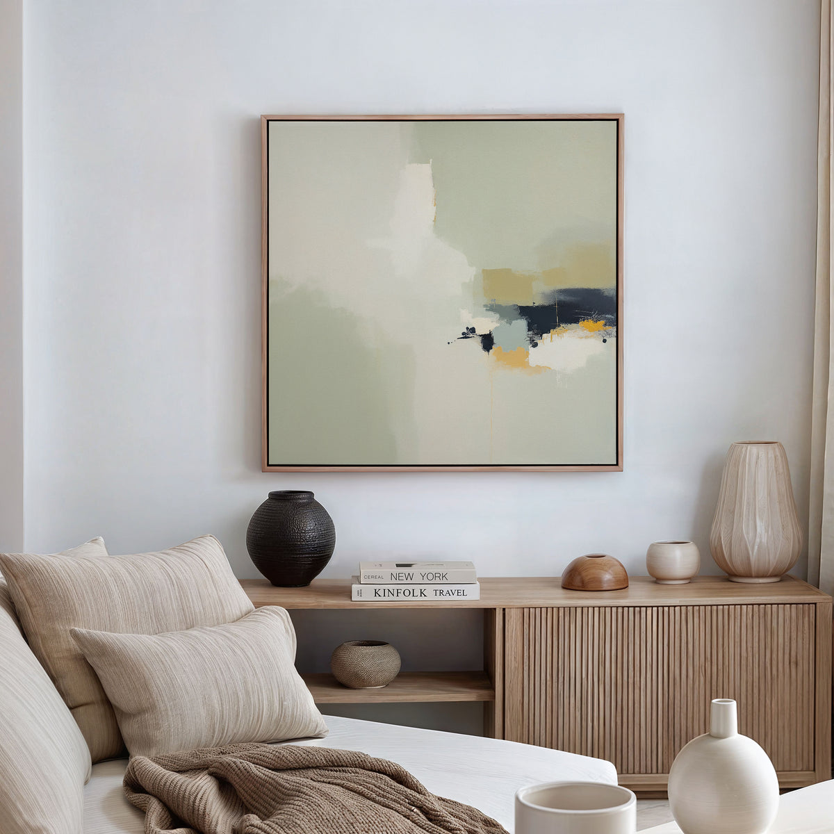 A modern living room featuring a beige sofa, neutral cushions, a wooden sideboard with vases and books, and the Weathered Composition Canvas Art - Square in soft hues on the wall exuding modern elegance.