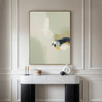 A modern console table with decor sits against a light-paneled wall, topped by the Weathered Composition Canvas Art - Vertical, a large abstract print in soft beige, white, navy, and gold tones that exude modern elegance.