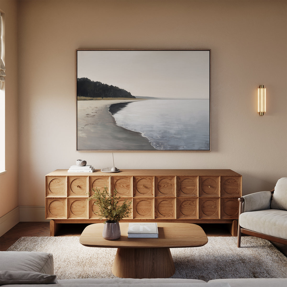 A minimalist living room with light walls, a wood sideboard, a coffee table, and a beige sofa features the Weathered Shore Canvas Art - Horizontal above the sideboard. A vase with flowers and books rest on the table.