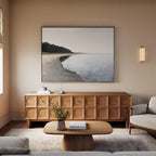 A minimalist living room with light walls, a wood sideboard, a coffee table, and a beige sofa features the Weathered Shore Canvas Art - Horizontal above the sideboard. A vase with flowers and books rest on the table.