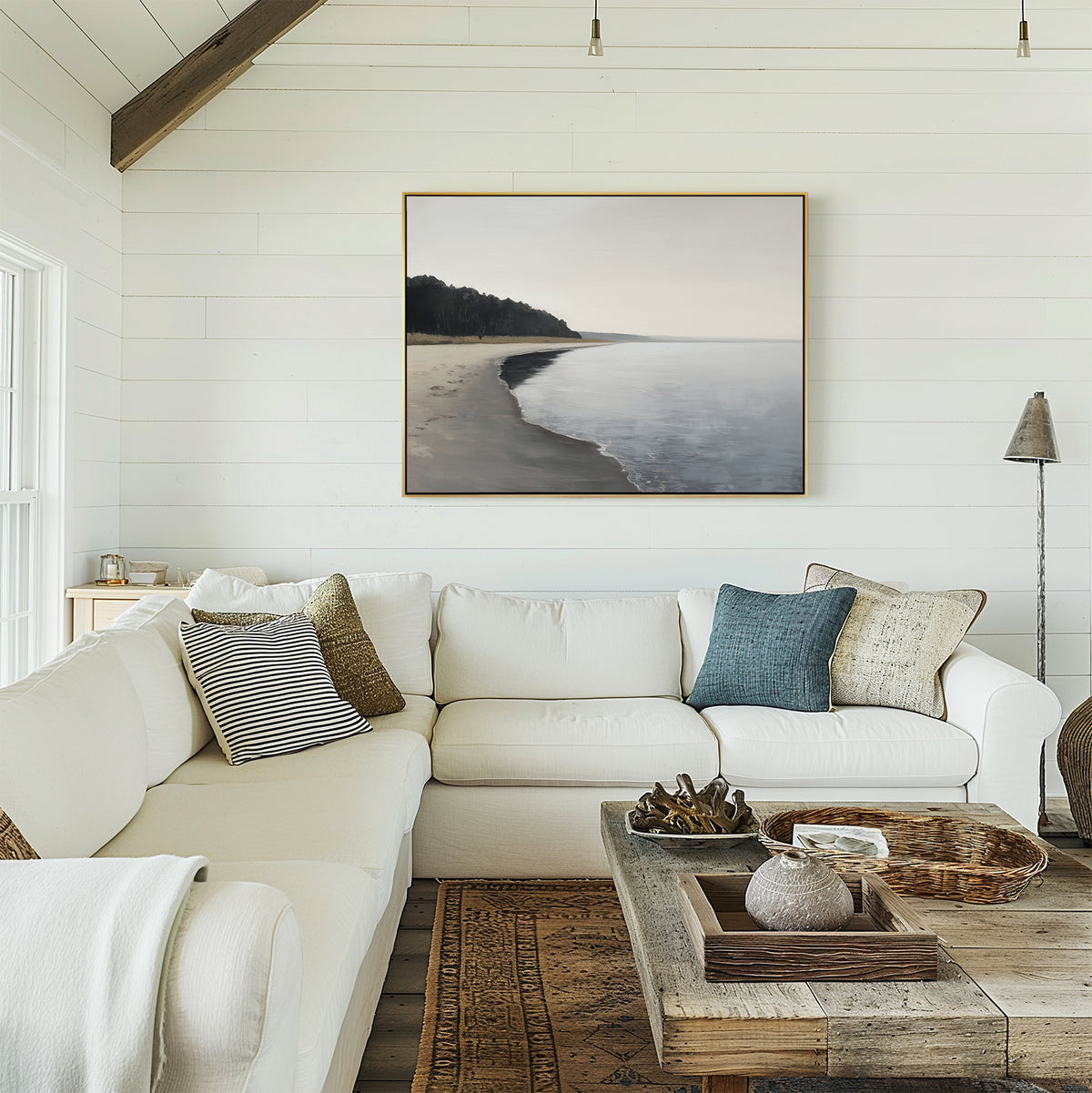 A cozy living room features a white sectional, textured pillows, a rustic wooden coffee table, and the Weathered Shore Canvas Art - Horizontal on shiplap walls. Sunlight streams in from a window to the left.