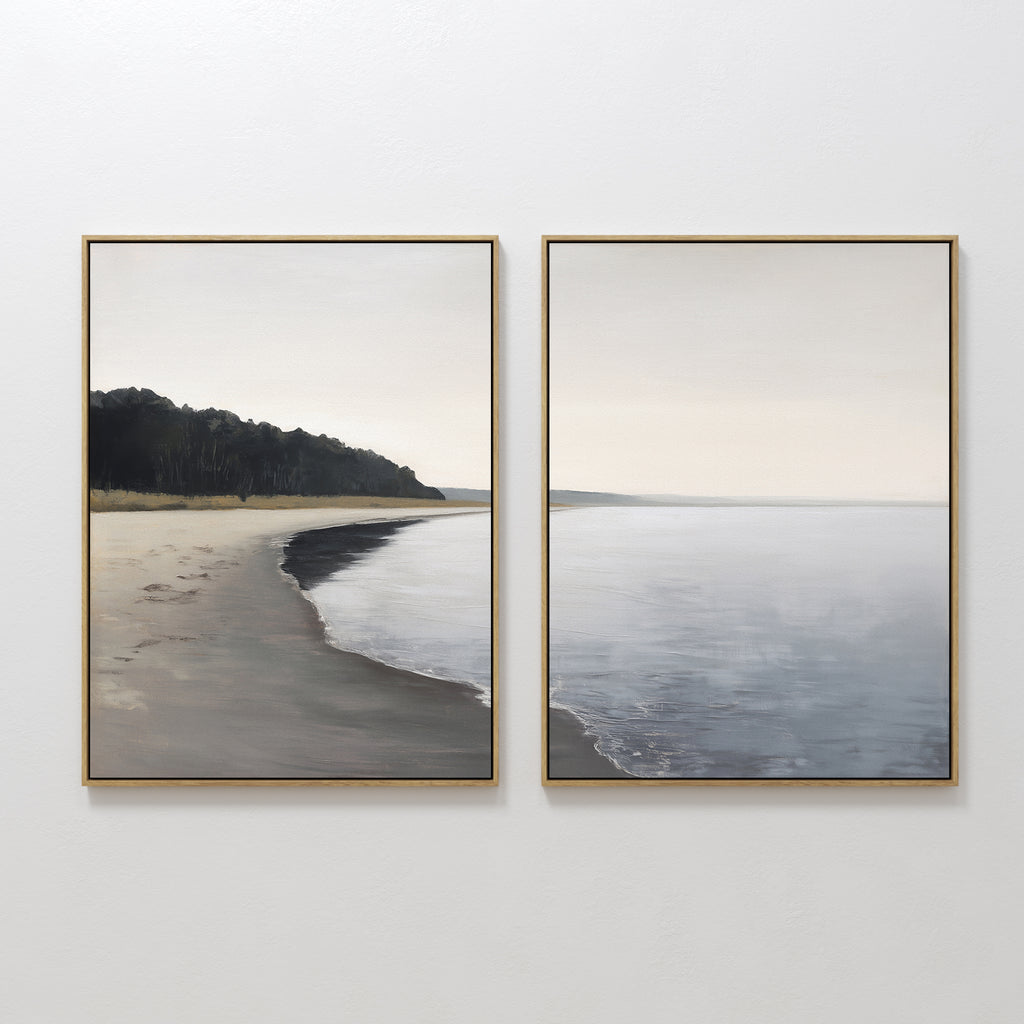 The Weathered Shore - Set of 2 features framed wall art depicting a calm beach with gentle waves and distant trees beneath a cloudy sky. Soft, muted colors create a serene, peaceful vibe—ideal for fans of tranquil coastal canvas prints.