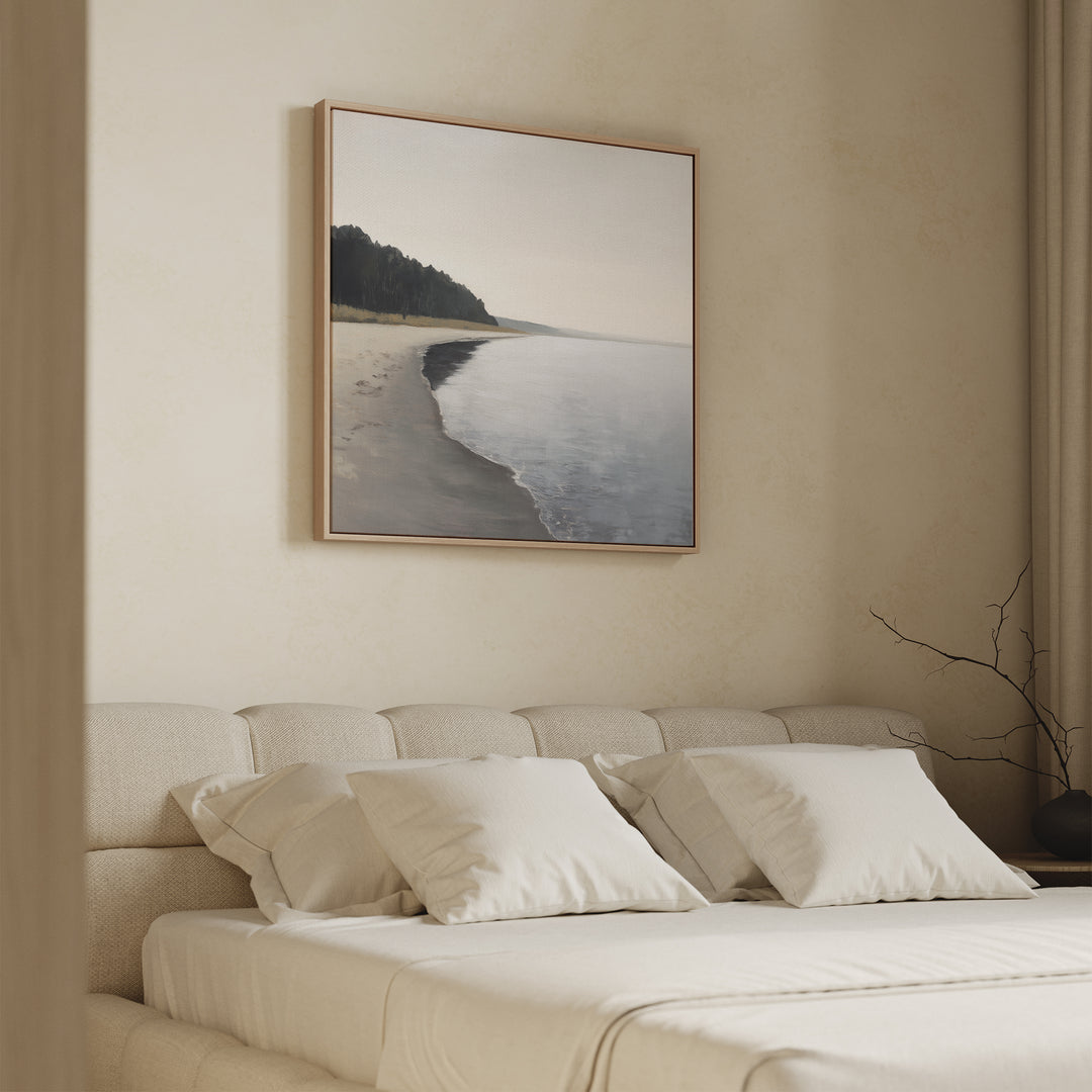 A minimalist bedroom features a beige upholstered bed, cream bedding, and the Weathered Shore Canvas Art - Square above the headboard. Neutral walls and a simple branch in a vase complete the calm, serene decor.