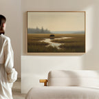 A person stands in a minimalistic, sunlit room, facing the Wetland Bear Canvas Art - Horizontal—a serene marshland scene with tall grass and water—displayed above a plush white sofa.