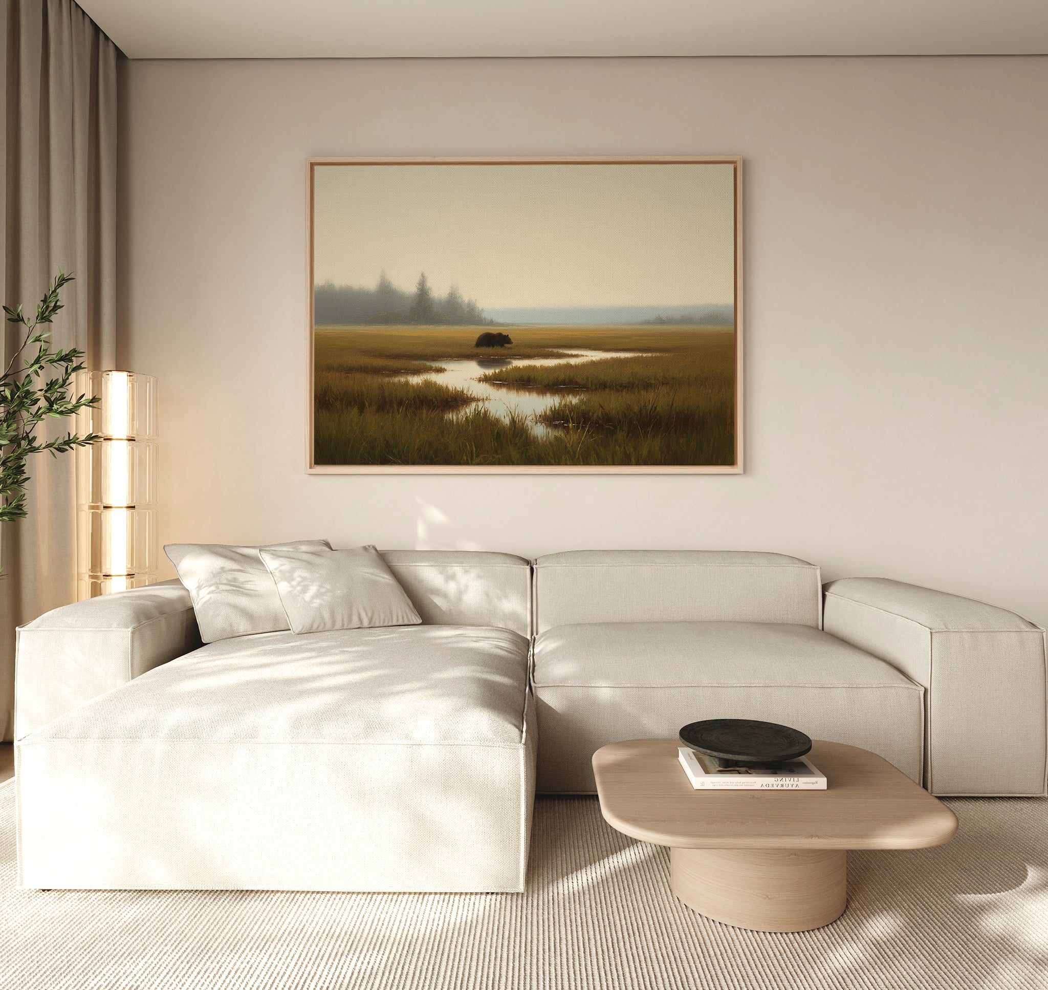 A modern living room featuring a light beige sectional sofa, wooden coffee table with a black bowl, tall plant, and the Wetland Bear Canvas Art - Horizontal depicting serene river and fields. Neutral tones and natural light create a tranquil atmosphere.