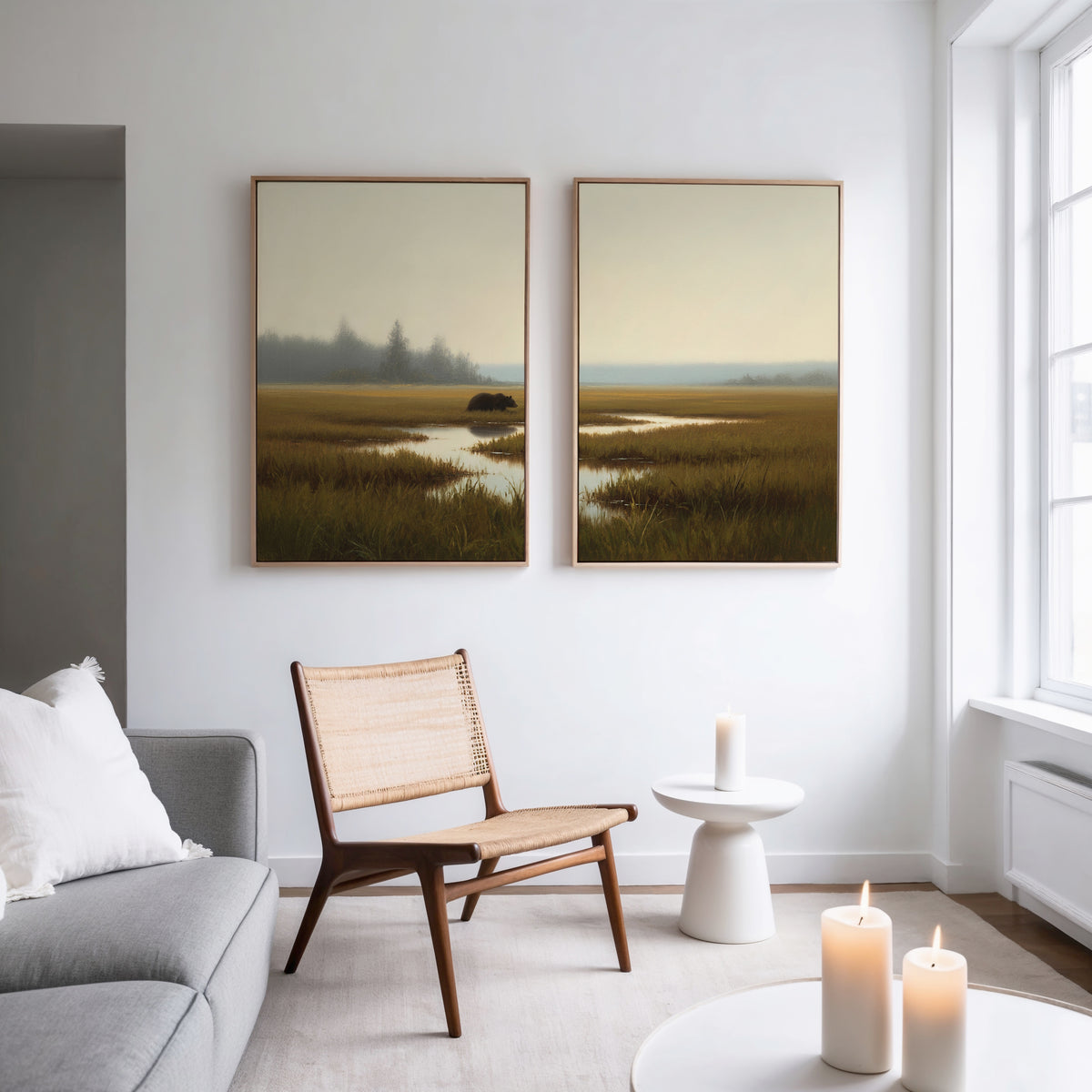 A modern, minimalist living room with a gray sofa, wooden chair, small white table, lit candles, and the Wetland Bear - Set Of 2 art on the wall. Natural light streams in from large windows.