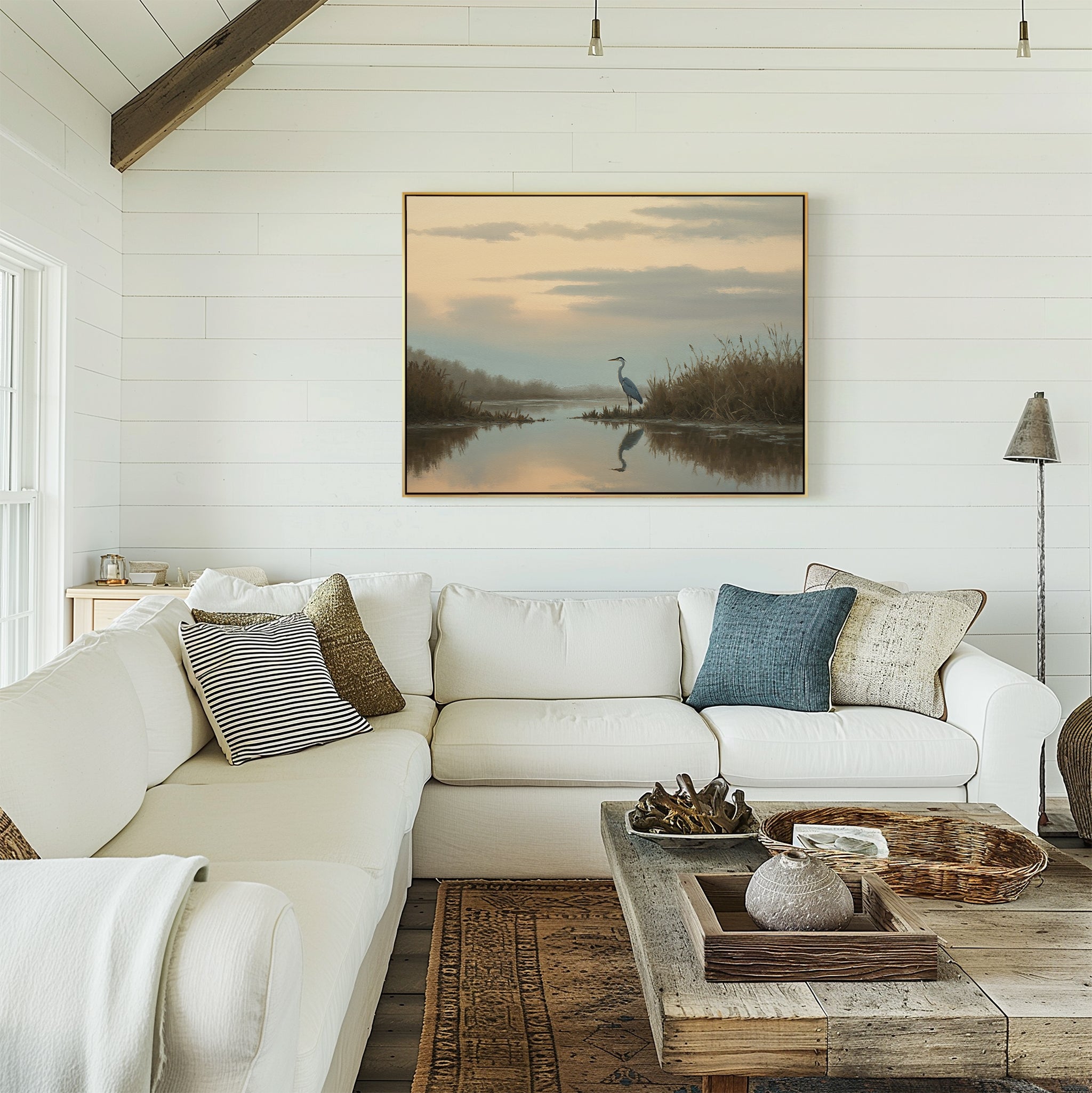 A bright, cozy living room with a white sectional sofa, assorted pillows, a rustic wooden coffee table, and the Wetland Heron Canvas Art - Horizontal featuring a marsh landscape decor on the shiplap wall.