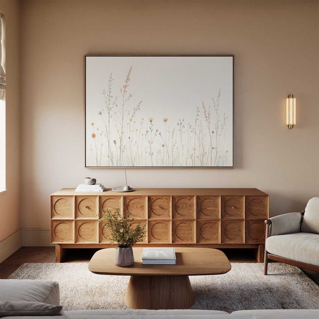 A cozy living room with light beige walls, a modern wooden sideboard, soft rug, neutral sofas, and a round coffee table with flowers is elevated by the Wildflower Dreams Canvas Art - Horizontal botanical wall art.