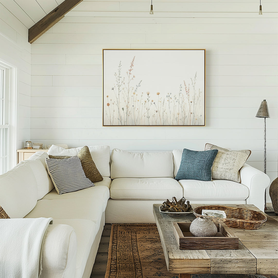 A cozy living room with a white sectional sofa, assorted pillows, a rustic wooden coffee table, and the Wildflower Dreams Canvas Art - Horizontal on a white shiplap wall. Natural light streams in from a window on the left.
