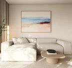A modern, minimalist living room with a beige sectional, light wood coffee table with a black bowl, tall plant, neutral walls and curtains, and the Windswept Coastline Canvas Art - Horizontal on the wall.