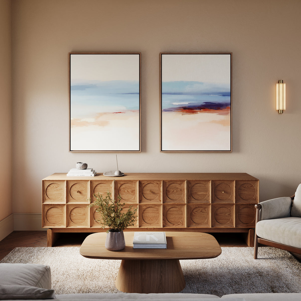 A modern living room features a wooden coffee table and sideboard, Windswept Coastline - Set Of 2 coastal wall art above the sideboard, a plant in a vase, neutral walls, and a cozy armchair.