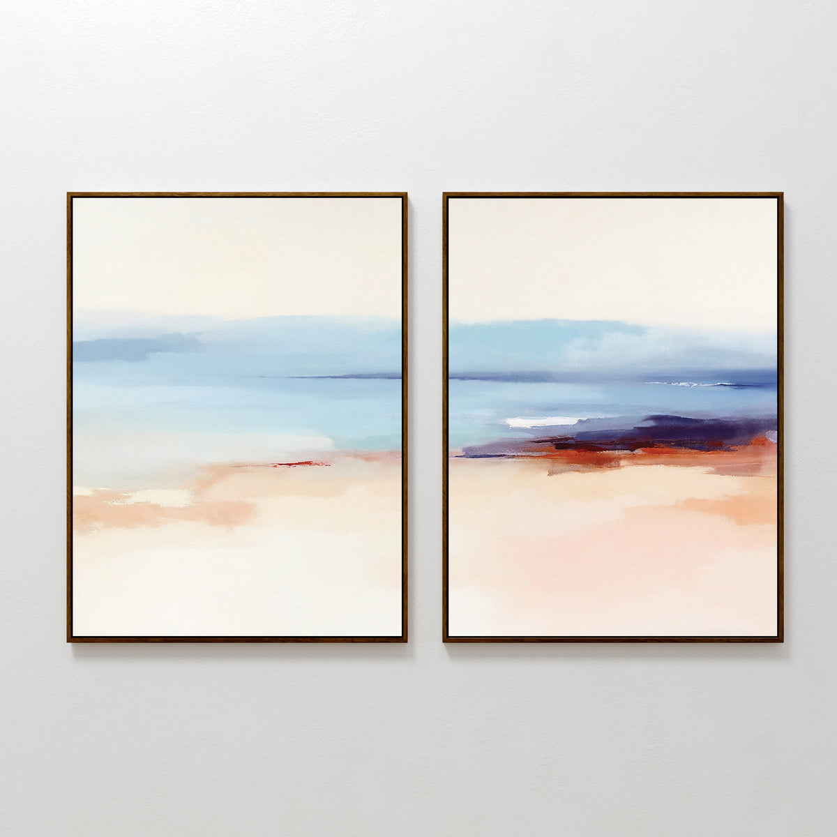 The "Windswept Coastline - Set Of 2" features two abstract prints side by side, showcasing soft, blurred landscapes in pastel blue, peach, cream, and touches of purple, evoking a calm seascape. Each piece is framed in dark wood.