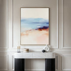 A minimalist room with a white paneled wall, a marble console table with decor, and the Windswept Coastline Canvas Art - Vertical in soft blue, beige, and coral tones above, creating a tranquil atmosphere.