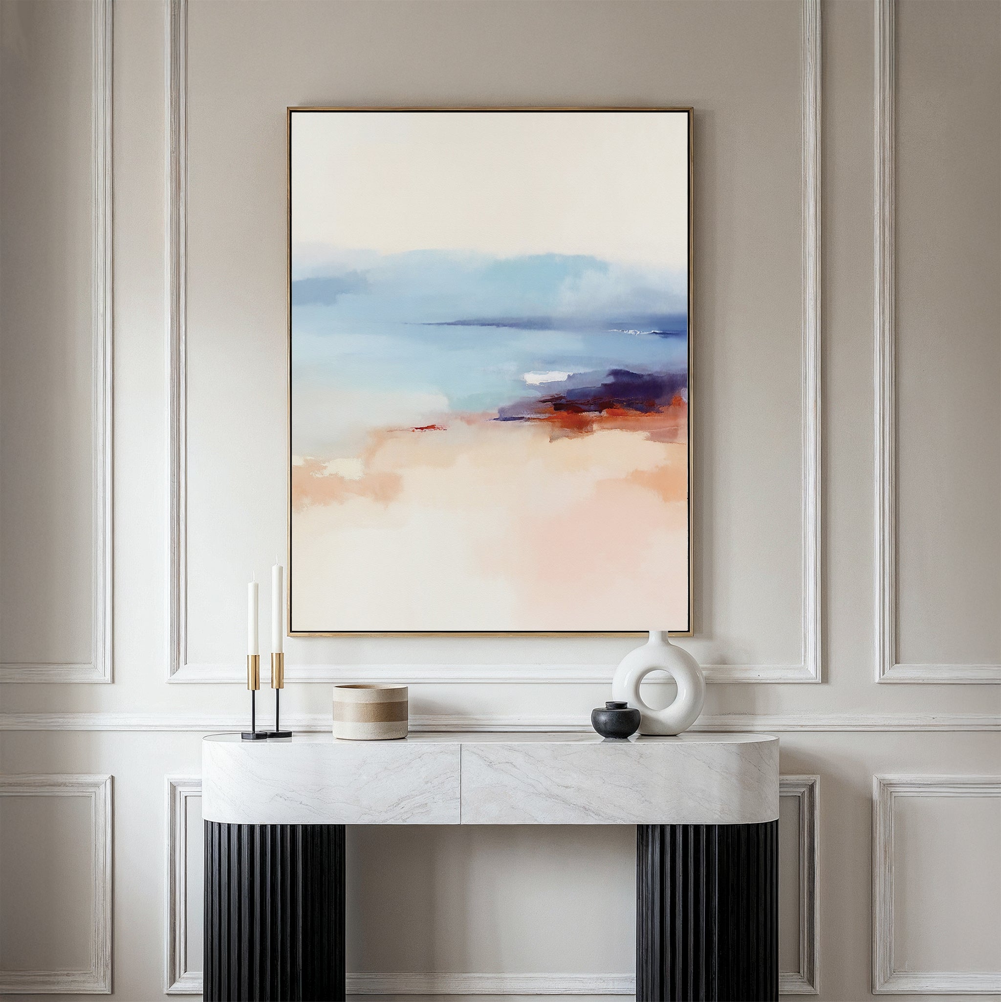 A minimalist room with a white paneled wall, a marble console table with decor, and the Windswept Coastline Canvas Art - Vertical in soft blue, beige, and coral tones above, creating a tranquil atmosphere.