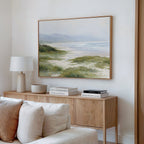 A living room with a light wood console table, stacked books, a white lamp, a bowl, and the Windswept Dunes Canvas Art - Horizontal above a cream-colored sofa creates a calming atmosphere.