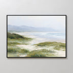 The Windswept Dunes Canvas Art - Horizontal showcases grassy sand dunes, a sandy beach, gentle waves, and misty mountains beneath a cloudy sky for a calming coastal atmosphere.
