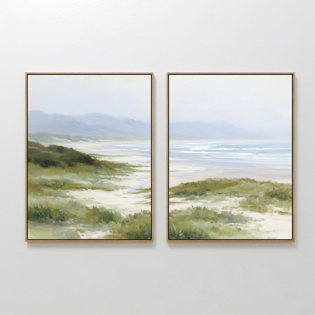 The Windswept Dunes - Set of 2 features framed landscape paintings of coastal grasslands, grassy dunes, a sandy beach, soft waves beneath a hazy sky, and gentle hills in the distance for a calming atmosphere.