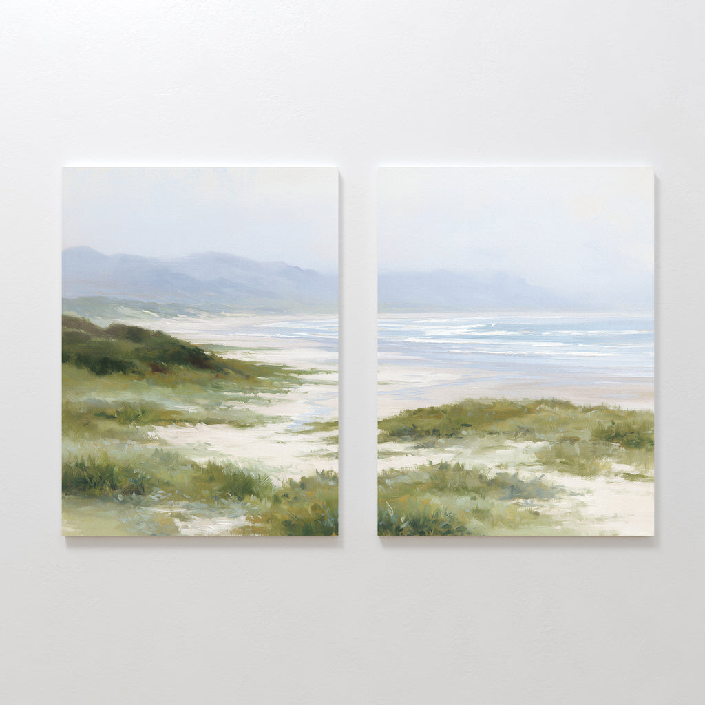 The "Windswept Dunes - Set of 2" features canvas paintings side by side, depicting a calm coastal landscape with sandy paths, grassy dunes, distant hills, and a tranquil ocean beneath a cloudy sky in soft, muted colors.