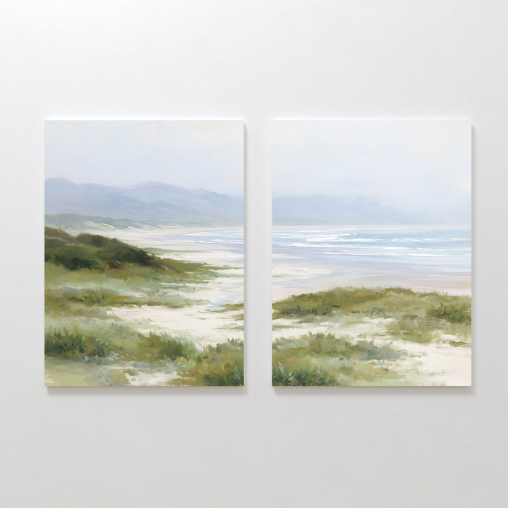The "Windswept Dunes - Set of 2" features canvas paintings side by side, depicting a calm coastal landscape with sandy paths, grassy dunes, distant hills, and a tranquil ocean beneath a cloudy sky in soft, muted colors.