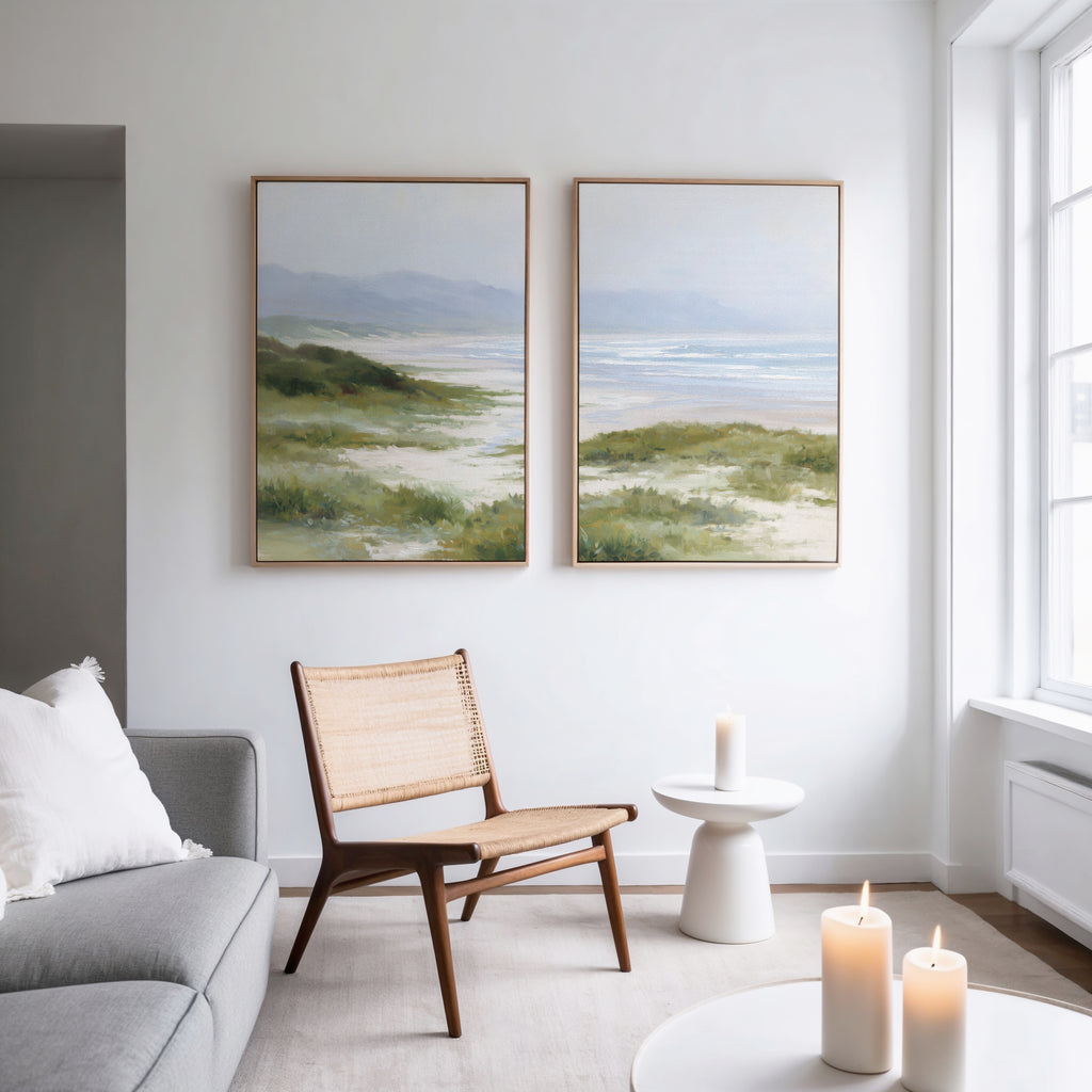A modern living room with a gray sofa, woven chair, small white table with candles, and the Windswept Dunes - Set of 2 canvas prints creates a calming vibe as natural light pours in through large windows.