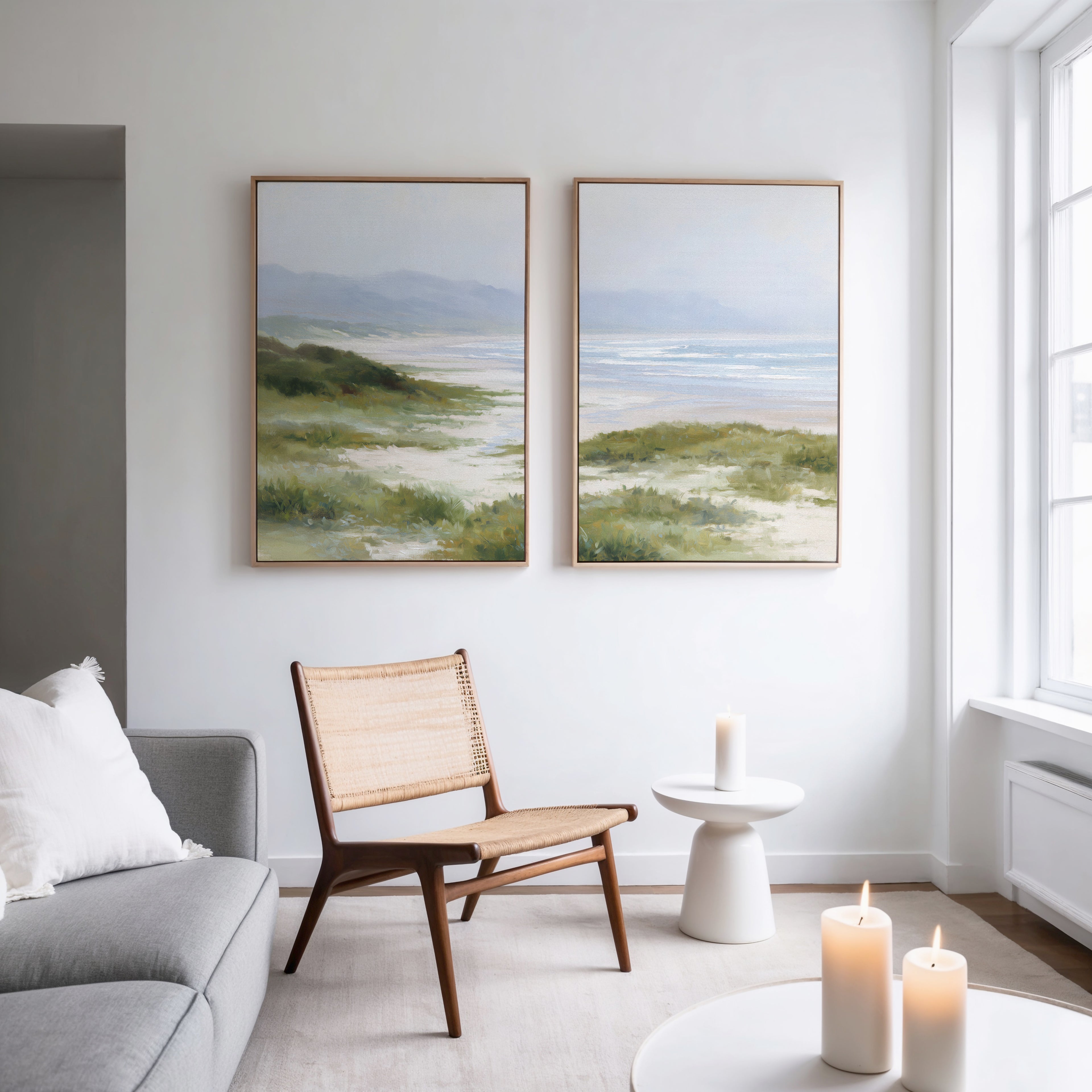 A modern living room with a gray sofa, woven chair, small white table with candles, and the Windswept Dunes - Set of 2 canvas prints creates a calming vibe as natural light pours in through large windows.