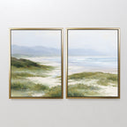 The "Windswept Dunes - Set of 2" framed canvas prints feature serene coastal grasslands, dunes, and a distant ocean under a cloudy sky, bringing a calming vibe to any plain white wall.