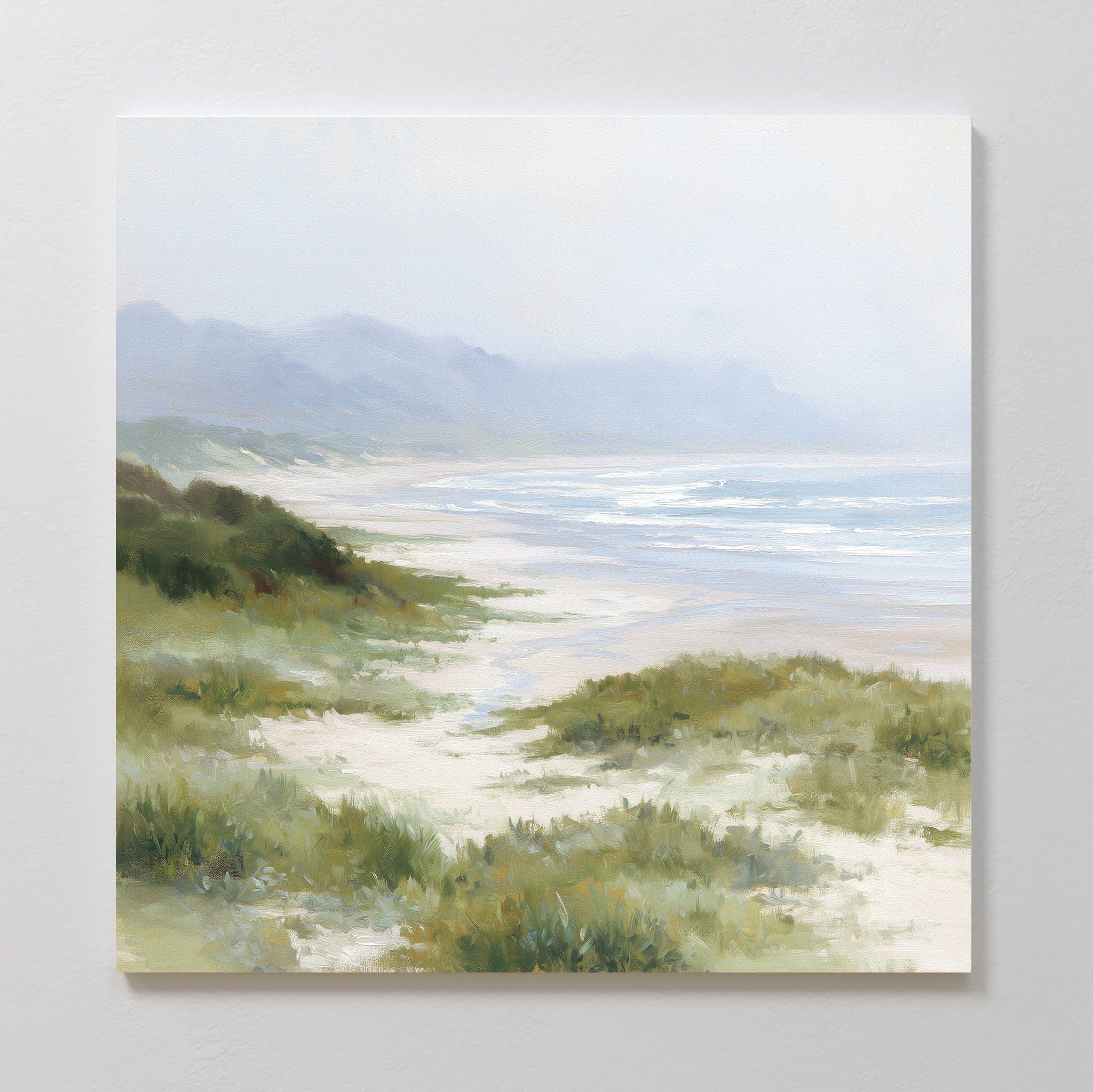 The Windswept Dunes Canvas Art - Square features sandy dunes, coastal grasslands, gentle waves, and misty mountains beneath a soft, cloudy sky, creating a serene and calming atmosphere.