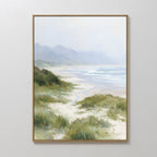 The Windswept Dunes Canvas Art - Vertical features a misty coastal landscape with grassy dunes, sandy beach, waves, and hazy mountains beneath a cloudy sky—ideal for adding calming decor to any space.