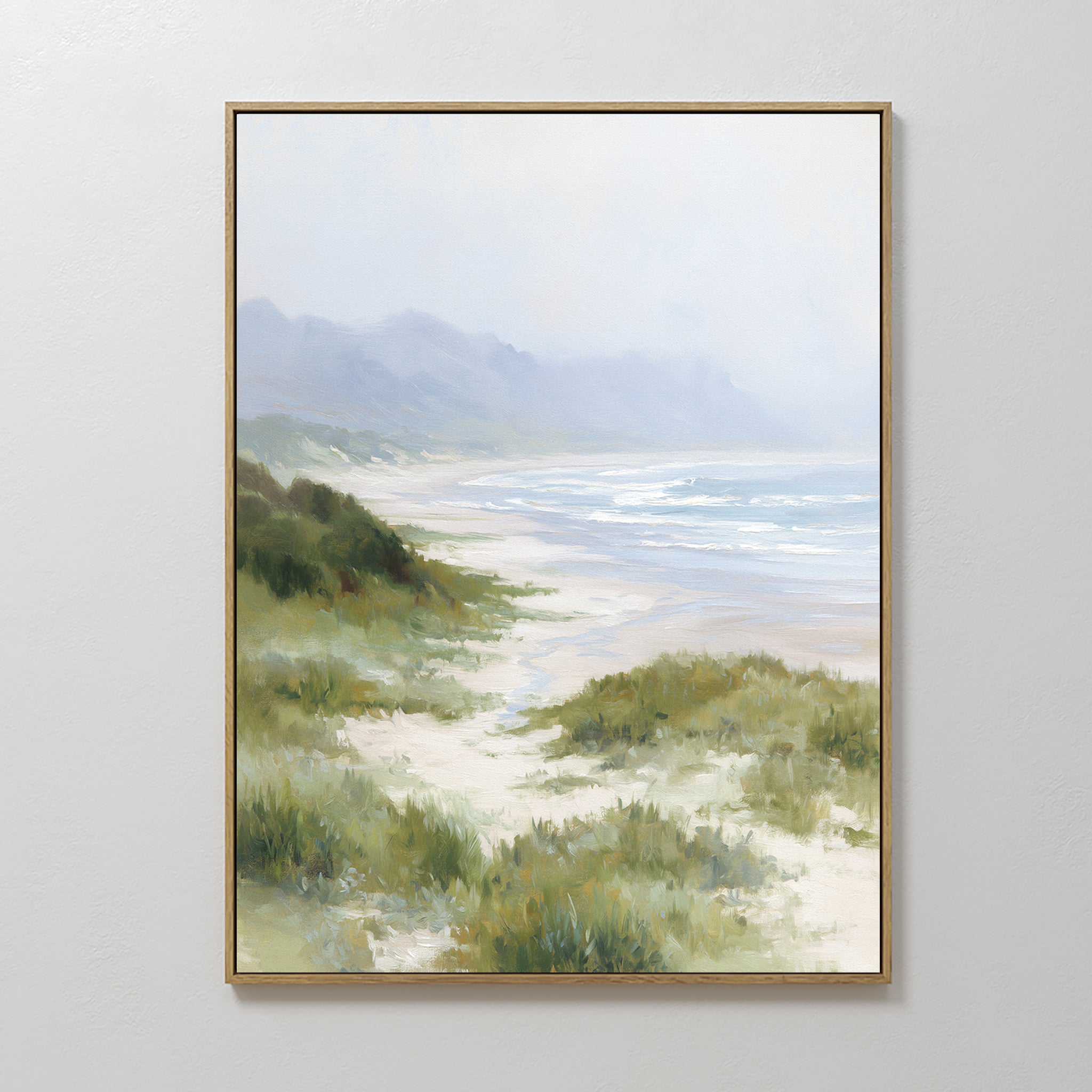 The Windswept Dunes Canvas Art - Vertical features a misty coastal landscape with grassy dunes, sandy beach, waves, and hazy mountains beneath a cloudy sky—ideal for adding calming decor to any space.