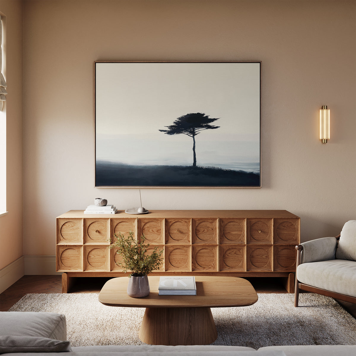 A minimalist living room with neutral tones features modern decor, including a wooden sideboard, coffee table, light sofa, wall-mounted light, and the Windswept Solitude Canvas Art - Horizontal above the sideboard.