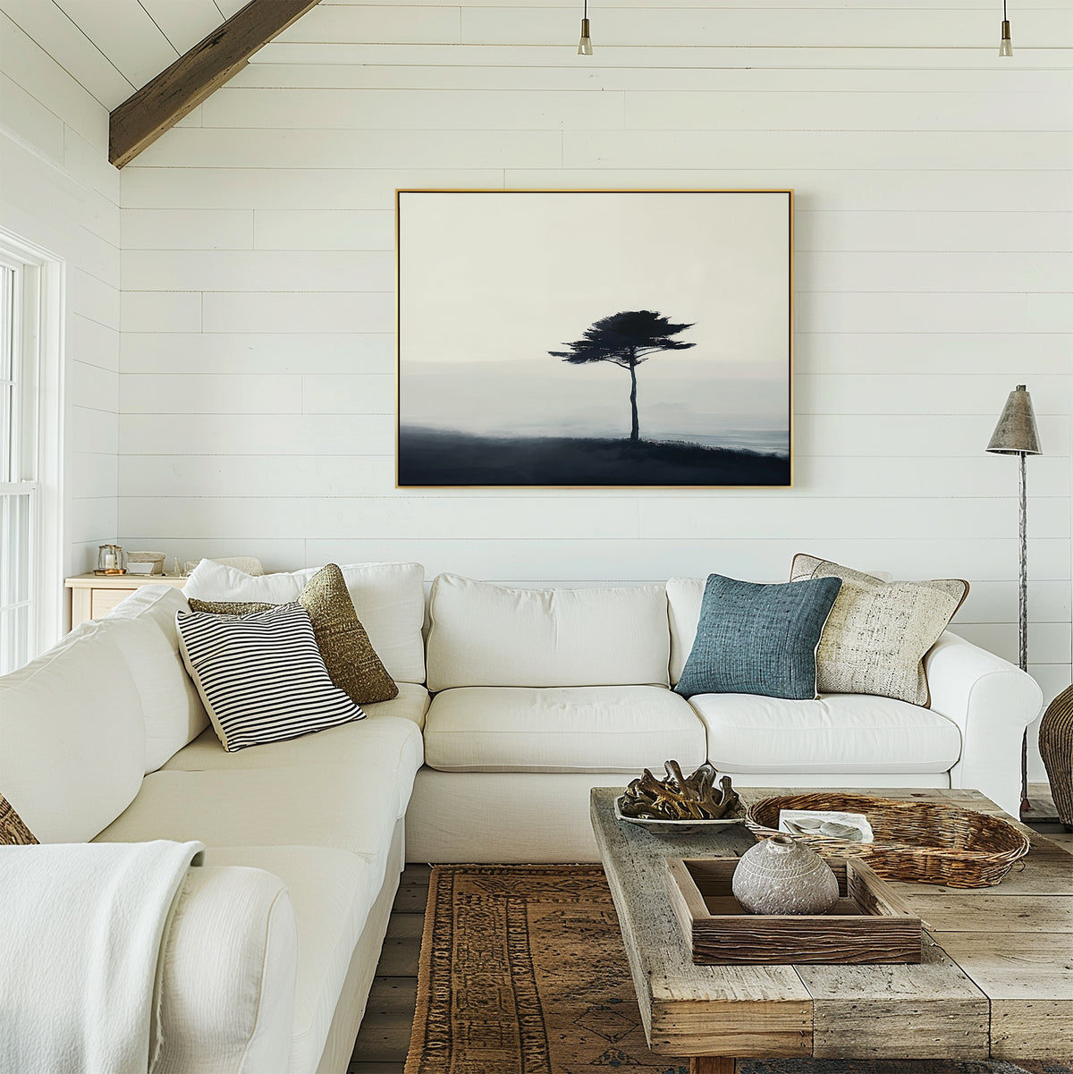 A cozy living room features a white sectional sofa, assorted pillows, a wooden coffee table, and the Windswept Solitude Canvas Art - Horizontal on a white shiplap wall. Natural light from the left enhances the modern decor.