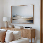 A modern living room with a light wood sideboard, white table lamp, books, and bowl is styled with the horizontal Winter Plains Canvas Art in soft neutrals above. A light-colored sofa anchors the foreground.