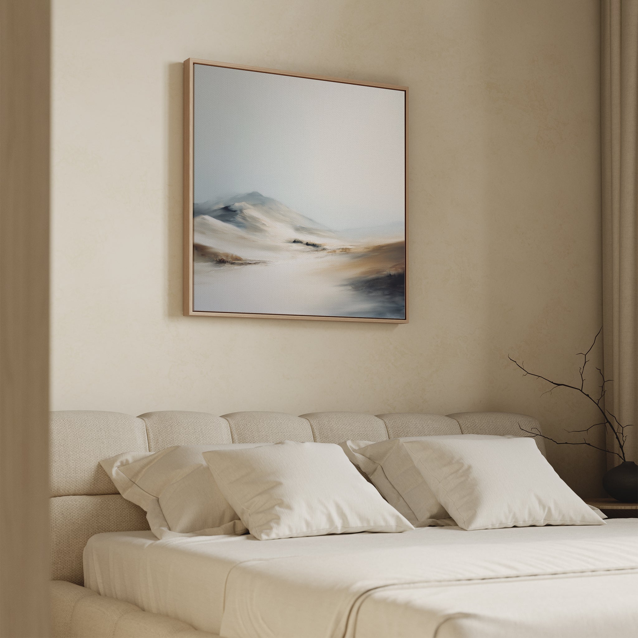 A softly lit bedroom with a beige bed, white pillows, and neutral bedding features the Winter Plains Canvas Art - Square above the bed—a serene abstract landscape in light blue, beige, and brown. A bare branch adorns the nightstand.