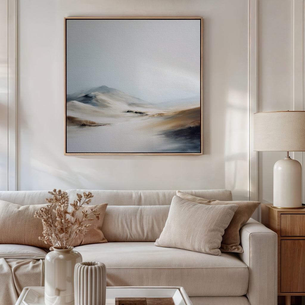 A modern living room with a beige sofa, neutral pillows, a side table and white lamp, dried flowers in a vase, and serene decor featuring the Winter Plains Canvas Art - Square framed on the wall.