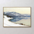 Winter Reflection Canvas Art - Horizontal features a tranquil snowy lakeshore with mountains, pine trees, a calm reflective lake, a pale sky, and tracks in the snow beside the water—ideal serene landscape wall decor.