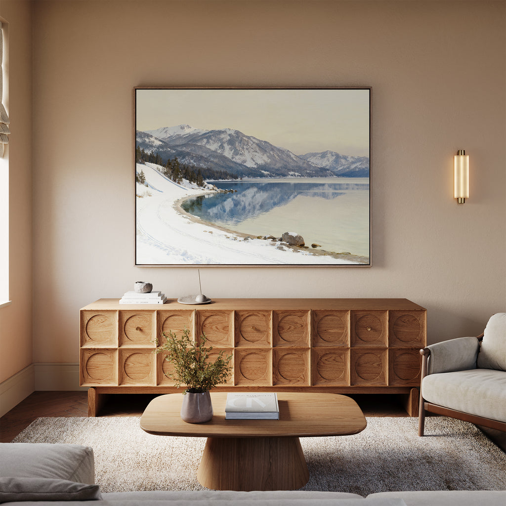 A cozy living room with neutral tones, featuring a wooden coffee table, sofa, sideboard, and a vase with greenery. Above the sofa hangs the Winter Reflection Canvas Art - Horizontal, adding a serene touch to the space.