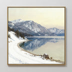 The Winter Reflection Canvas Art - Square features a framed print of snowy mountains, an alpine lake mirroring the peaks, a winding path lined with trees, and rocks by the shore beneath a pale winter sky.