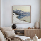 A cozy living room featuring a beige sofa, neutral cushions, and a wooden sideboard with vases and books. Above the sideboard hangs the Winter Reflection Canvas Art - Square, showcasing a snowy mountain reflected in an alpine lake.