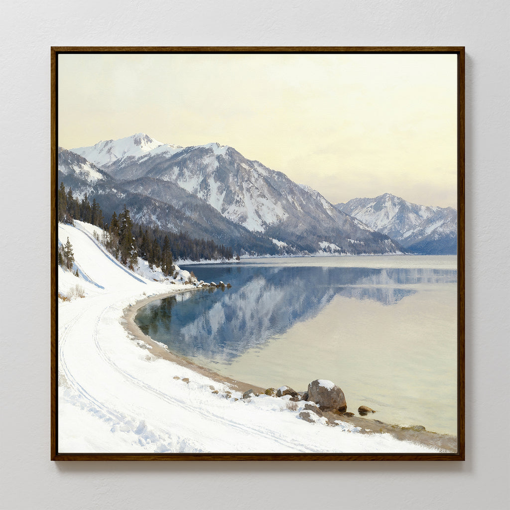 The Winter Reflection Canvas Art - Square features a snowy mountain landscape with pine trees, a winding snow-covered road, and a calm lake reflecting the mountains and sky under soft, diffused light.