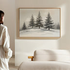 In a minimalistic room, a person admires the Winter Solitude Canvas Art - Horizontal, featuring snowy pine trees, hanging above a beige sofa on a light-colored wall.