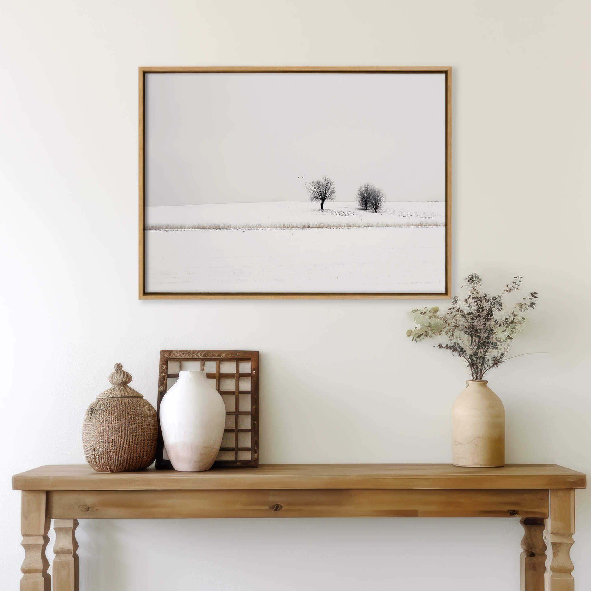A wooden console table with vases and decor stands against a white wall, above which hangs the Winter Silence Canvas Art—a minimalist photograph of snowy trees—creating the perfect winter decor.
